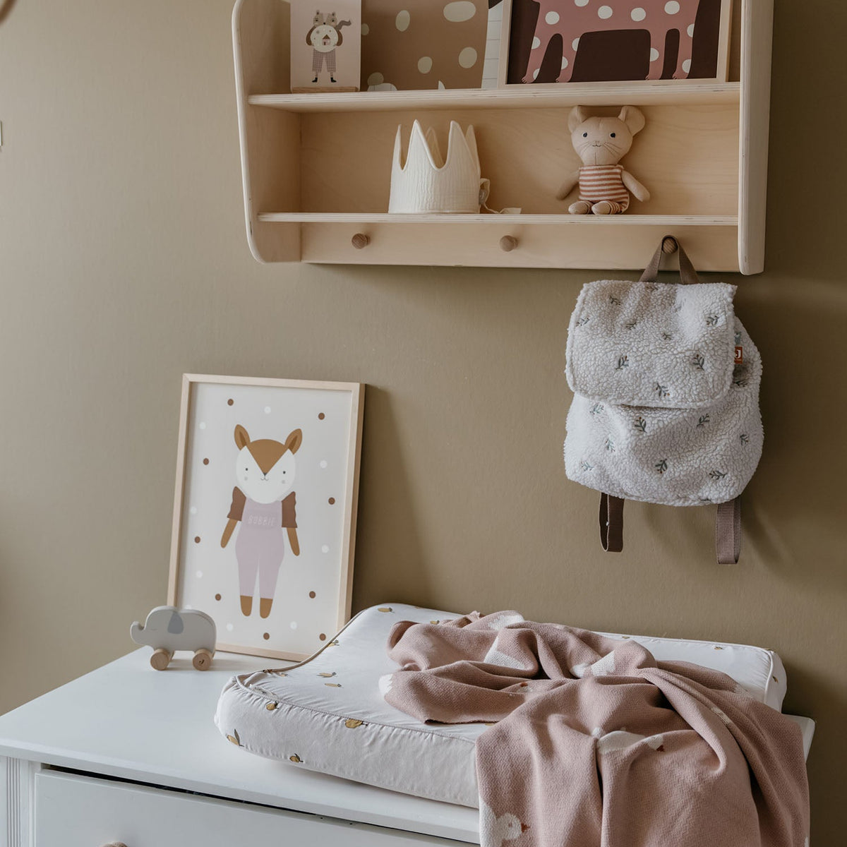 Nursery room with wooden shelf, baby items, and wall decorations on a beige wall.