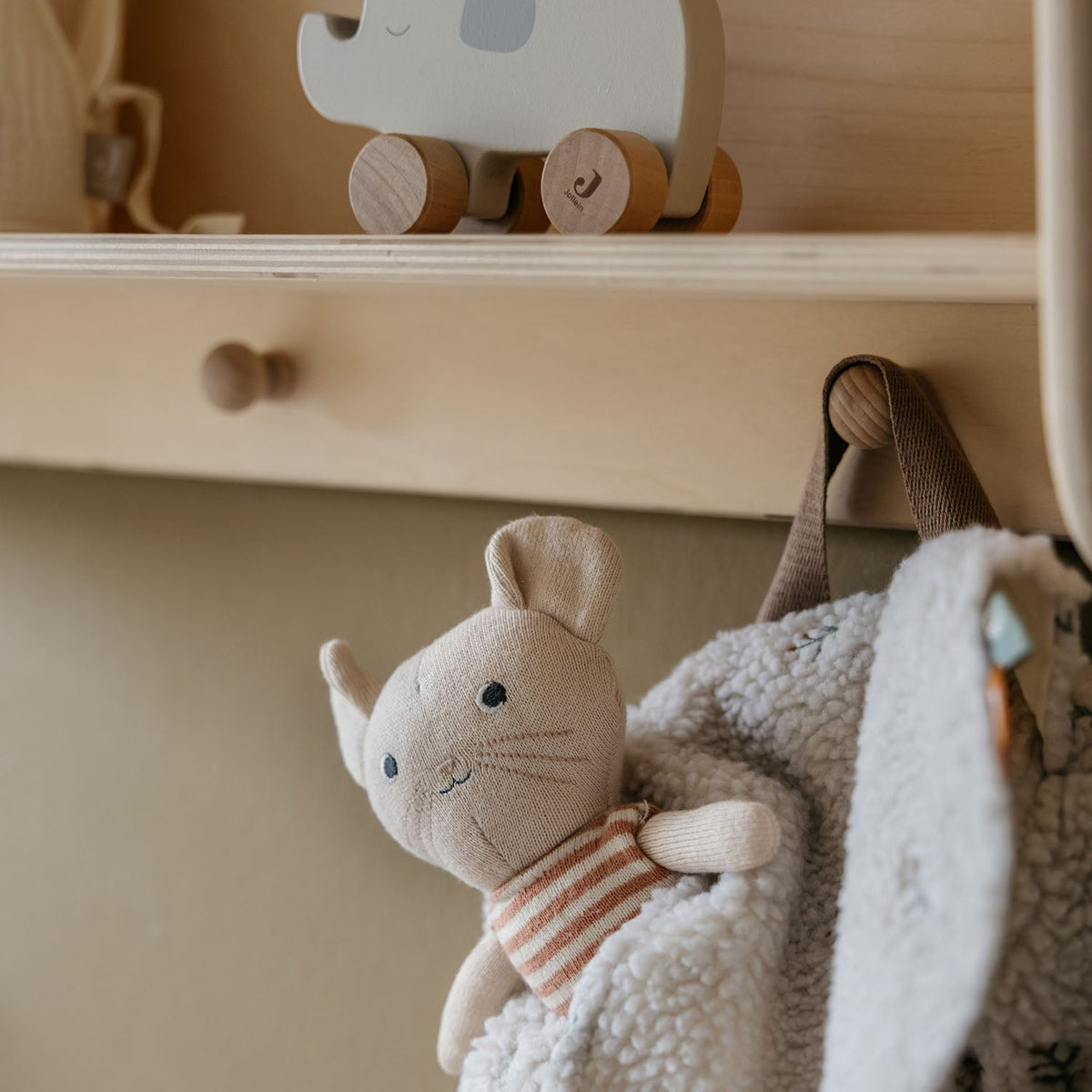 Children's room with a shelf holding a wooden elephant toy and a plush mouse toy hanging on a hook.