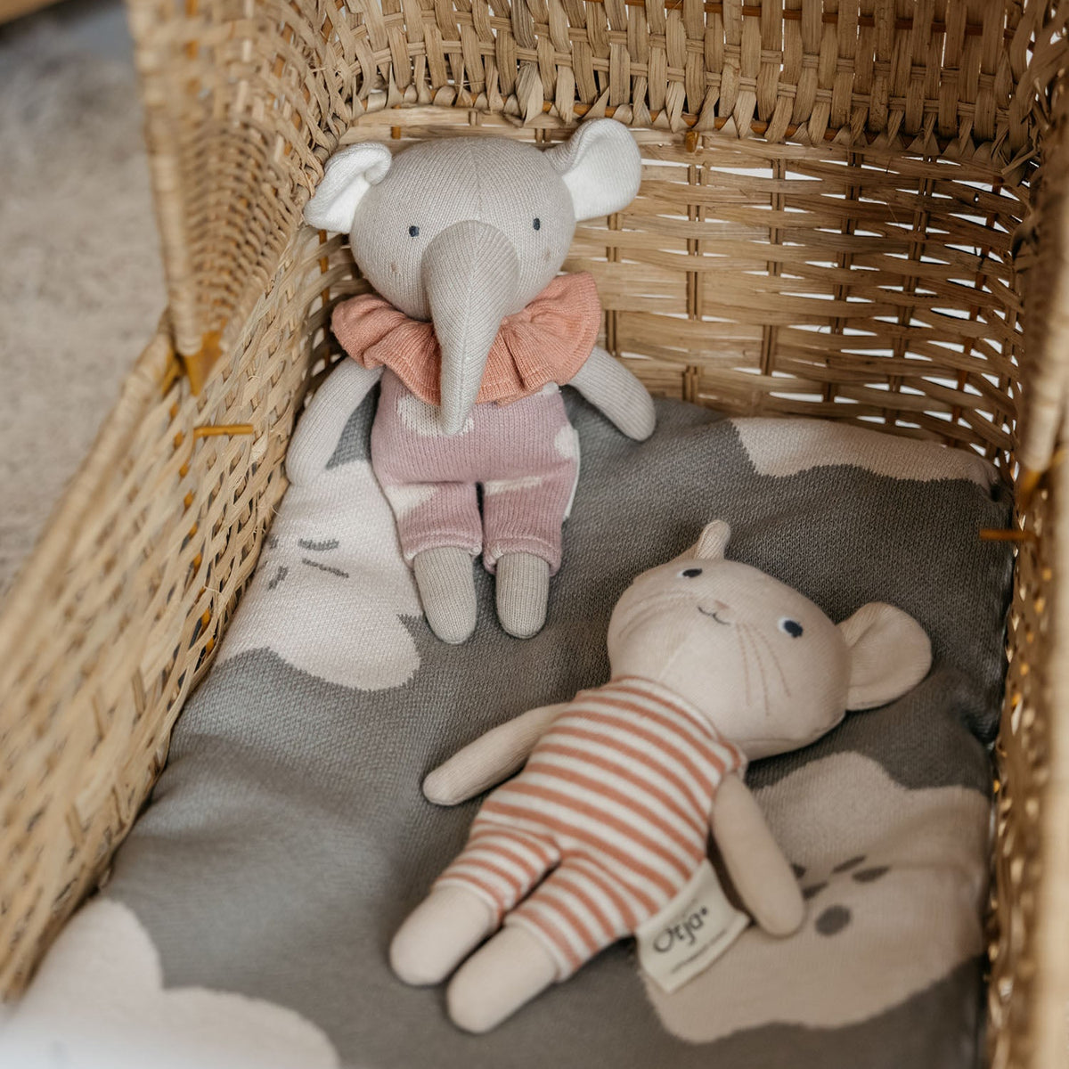 Wicker basket with plush toys including an elephant and a bear on a soft surface.