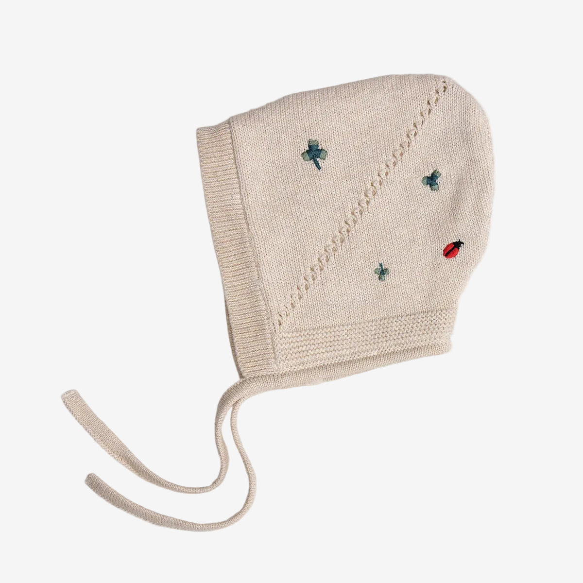 Beige knitted baby bonnet with embroidered ladybugs on a white background