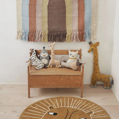 Children's room with a woven rainbow wall hanging, wooden bench, and animal plush toys.