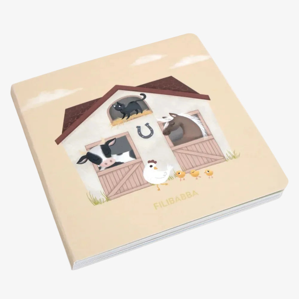 A square baby book with a cream-colored cover featuring a farm illustration of a stable with cows, a horse, a chicken, and chicks, and the name 'FILIBABBA' printed at the bottom.