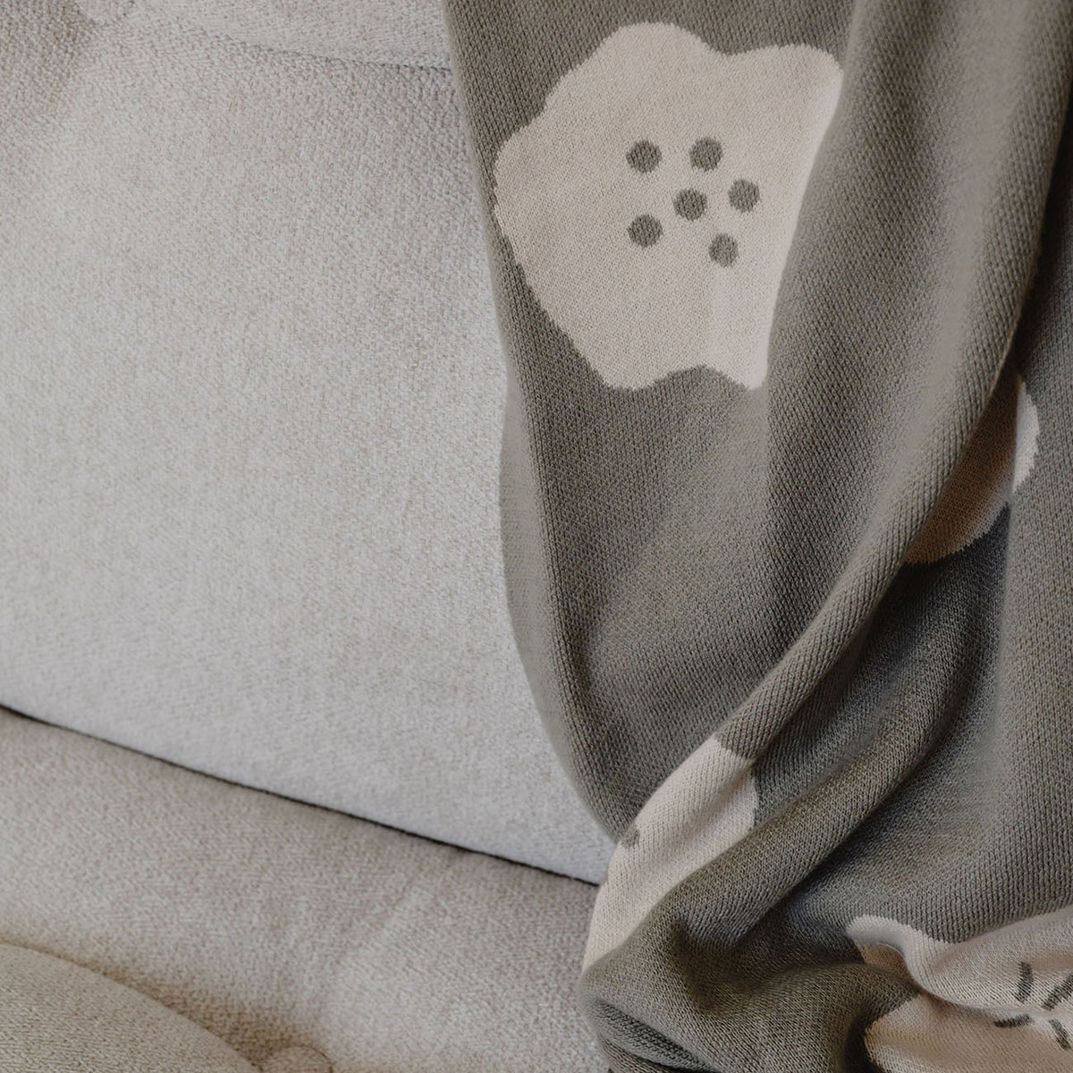 Gray blanket with floral pattern draped over a beige sofa