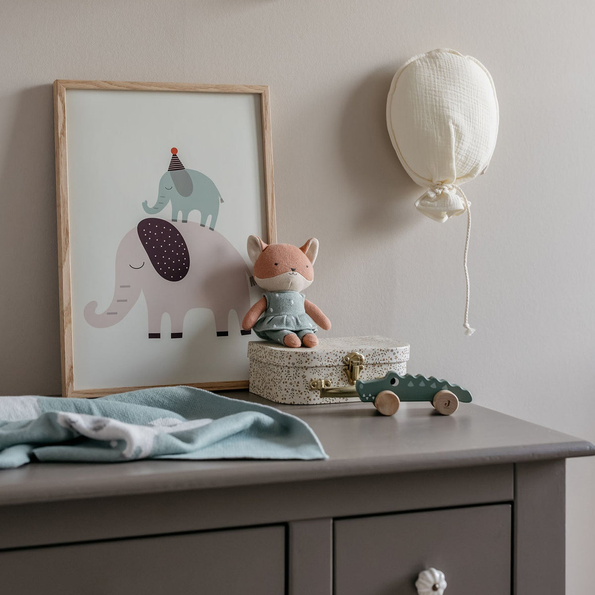 Nursery room with shelves, toys, and wall art on a light gray wall.