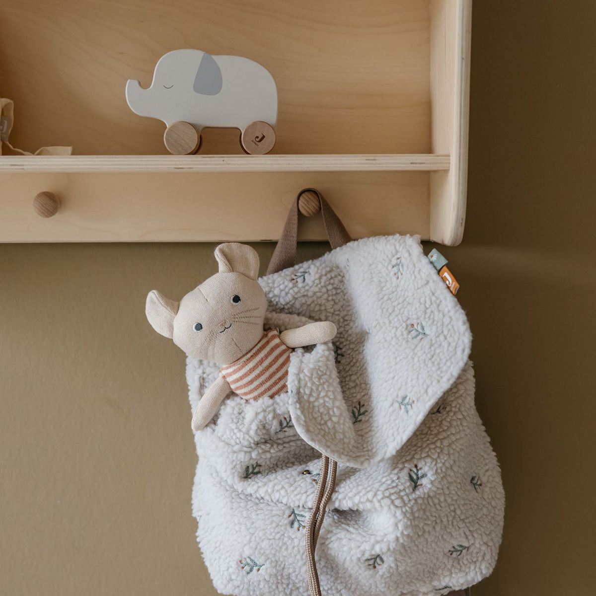 Backpack with plush toy attached to a wooden shelf against a beige wall