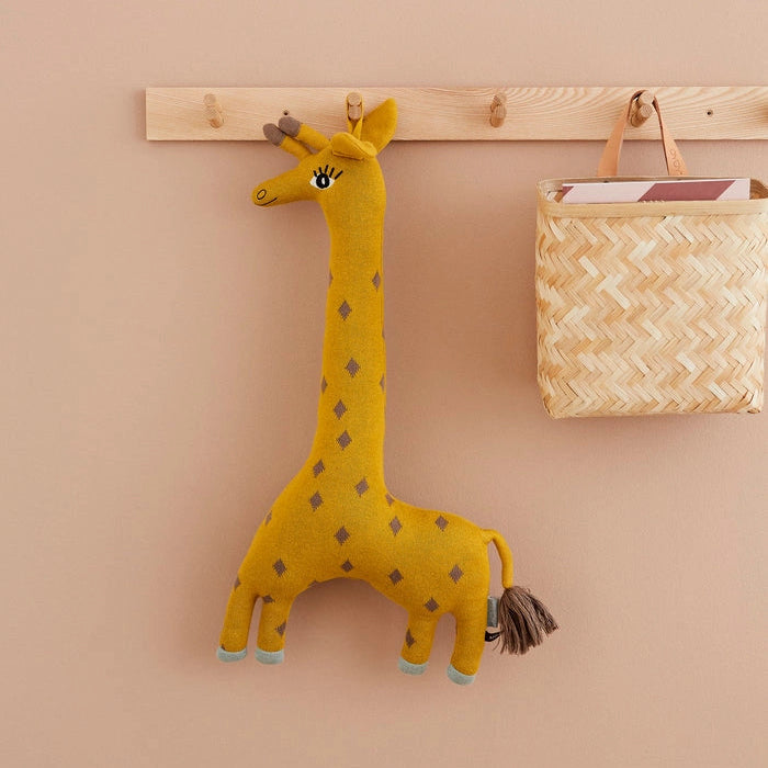 Yellow stuffed giraffe toy hanging on a wooden peg rack against a beige wall.