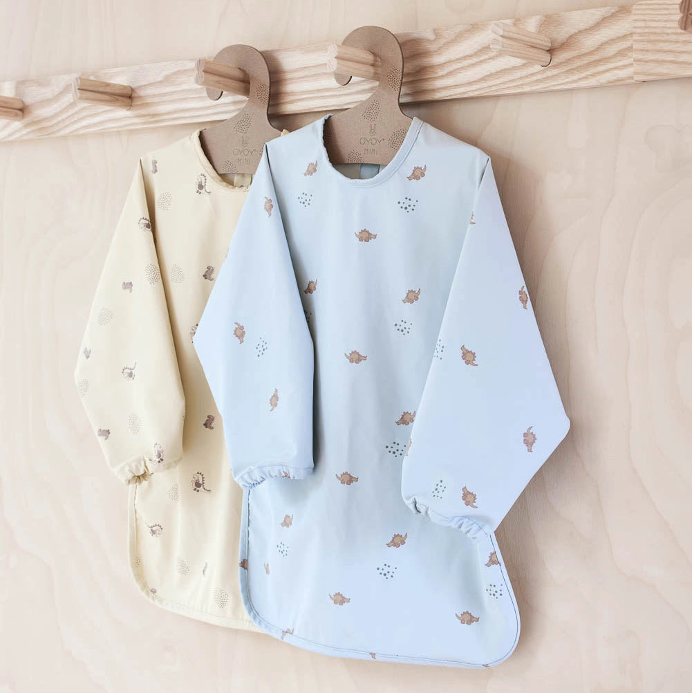 Two baby bibs, one cream and one light blue with floral patterns, hanging on a wooden rack.