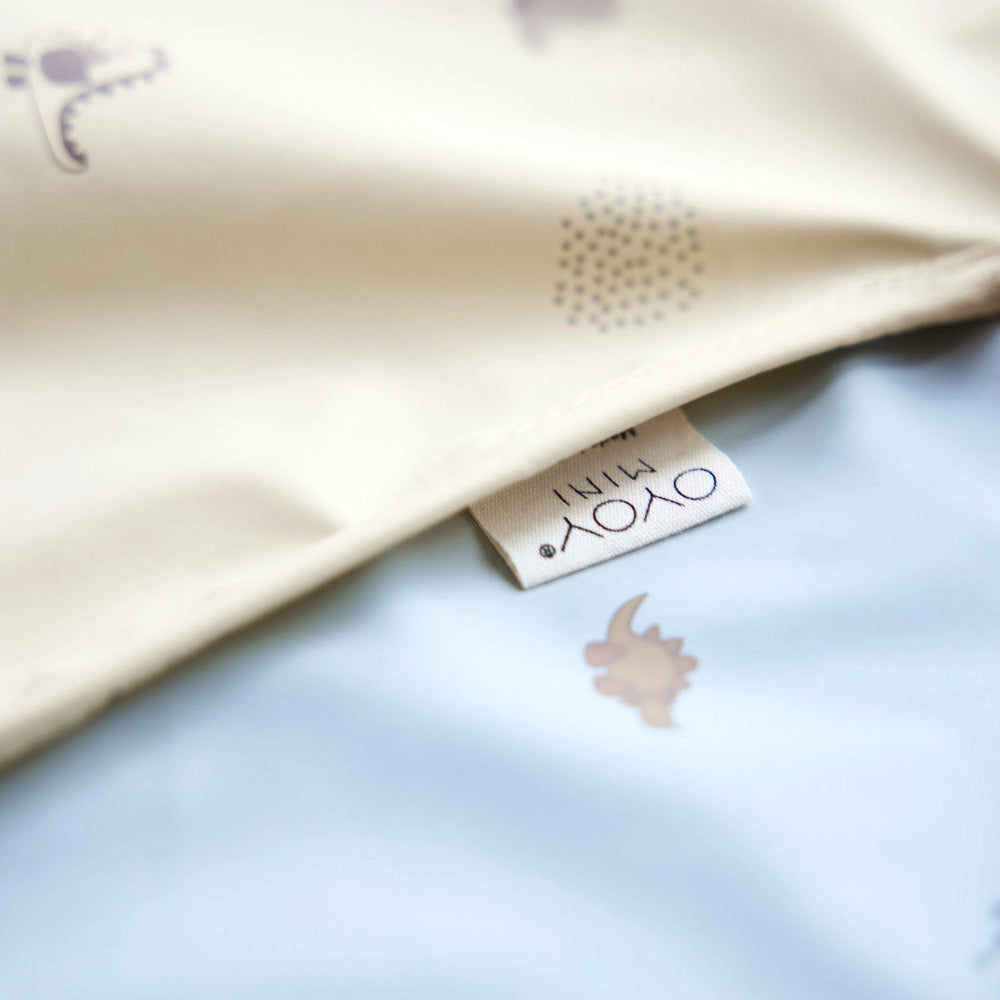 Close-up of fabric with small animal prints on a light blue background, featuring a brand tag.