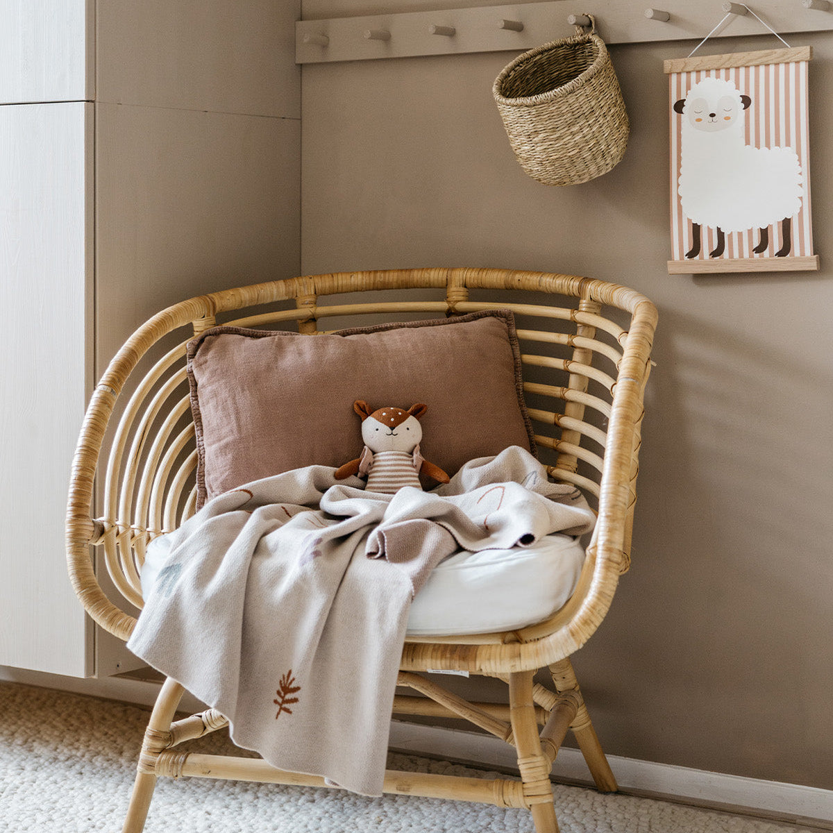 Wicker chair with a pillow and blanket in a room with a wall-mounted basket and framed picture.